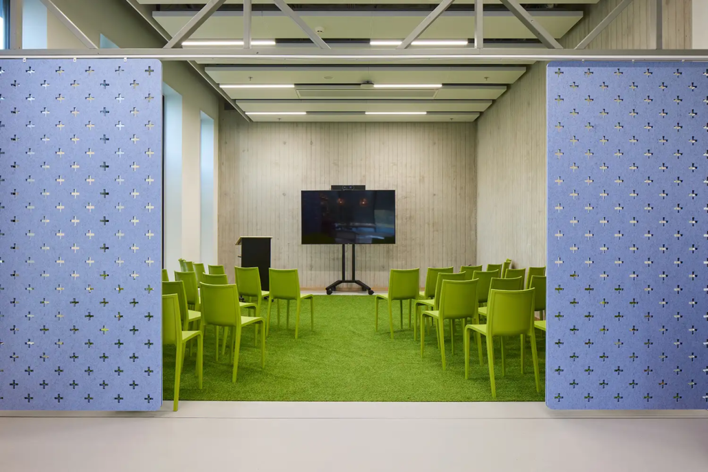 Mindlabs is een ruimte met een grasgroen tapijn, groene stoelen en een grote tv, die met blauwe panelen afgesloten kan worden.