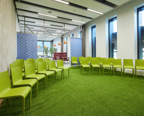 Groene stoelen geplaatst in een halve cirkel in een ruimte met een grasgroen tapijt