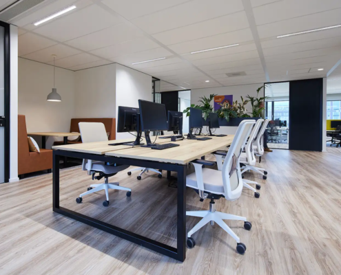 Ruimte voor studie en werken met grote tafel met houten blad en computers waaraan royale witte bureaustoelen staan.