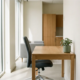 Moderne houten bureau met ergonomische stoel, daglicht door vloer-tot-plafondvensters en kleine kamerplant in een rustig kantoor.