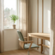 Lege consultatieruimte met ergonomische stoel, houten bureau, linnen gordijnen en potplant op de vensterbank in natuurlijk daglicht.