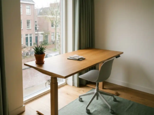 Zit-sta bureau met eikenhouten blad en ergonomische stoel bij raam met uitzicht op Nederlandse straat, klein potplantje op bureaurand.