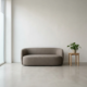 Minimalistische receptieruimte met grijze lage bank, houten bijzettafel met plant en betonlook vloer in natuurlijk daglicht.