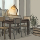 Rommelige Nederlandse kantoorhoek met stapels ordners, niet-bij-elkaar-passende stoelen en een hangende plant bij een smal bureau.